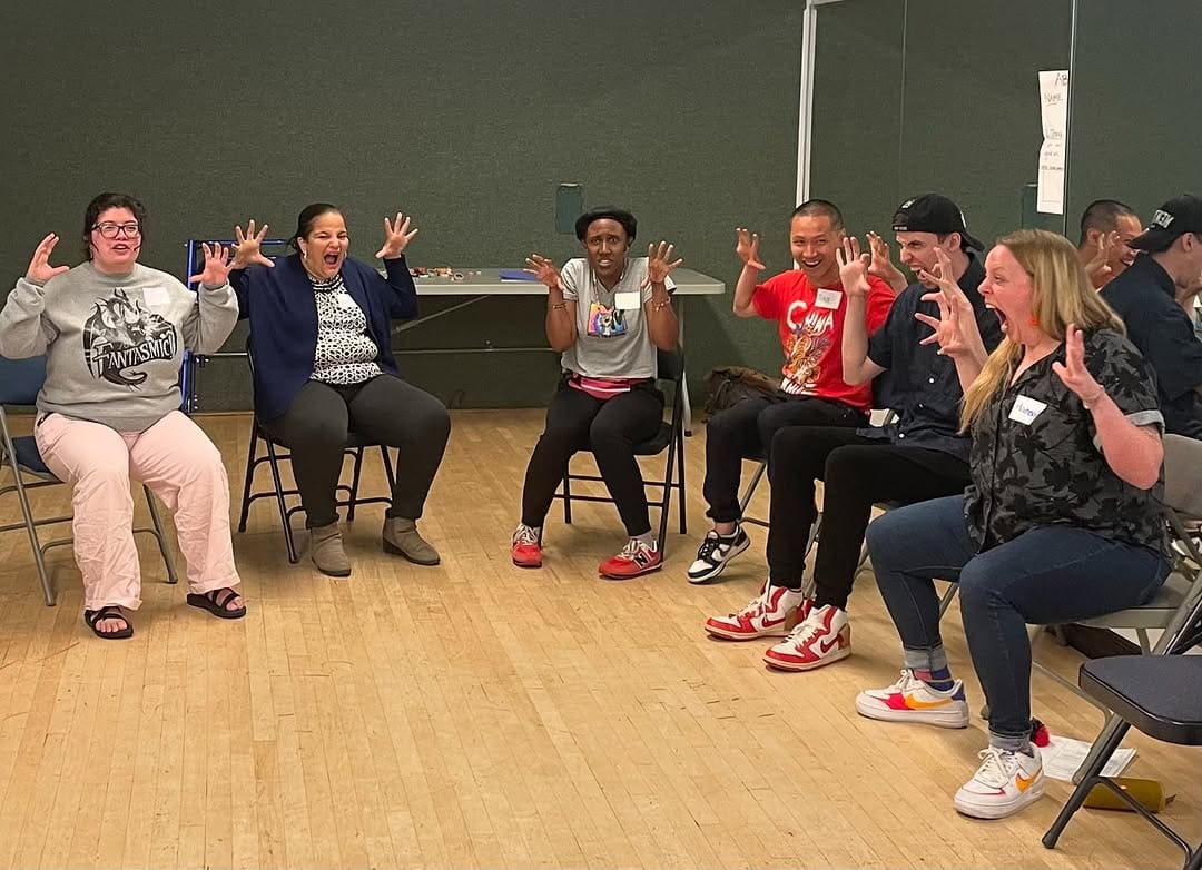 Group of people in a workshop, hands raised in surprise. Access Success.