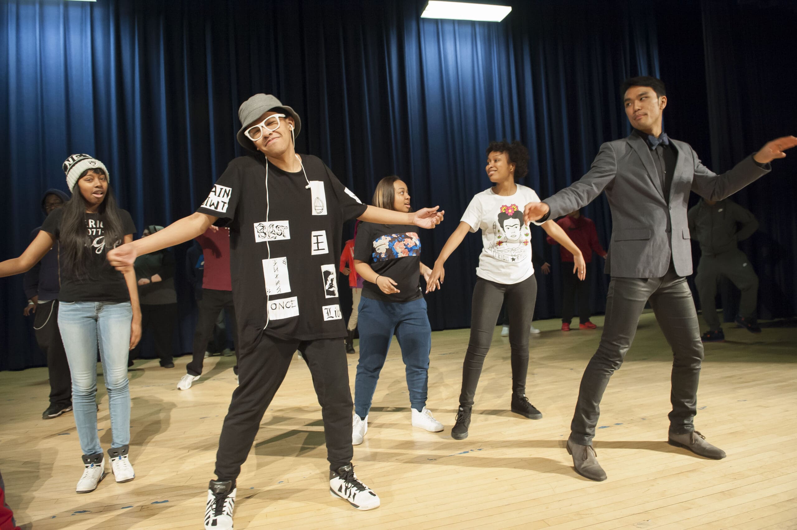 Dancers performing on stage, including a man in a suit and a woman in a shirt with text.