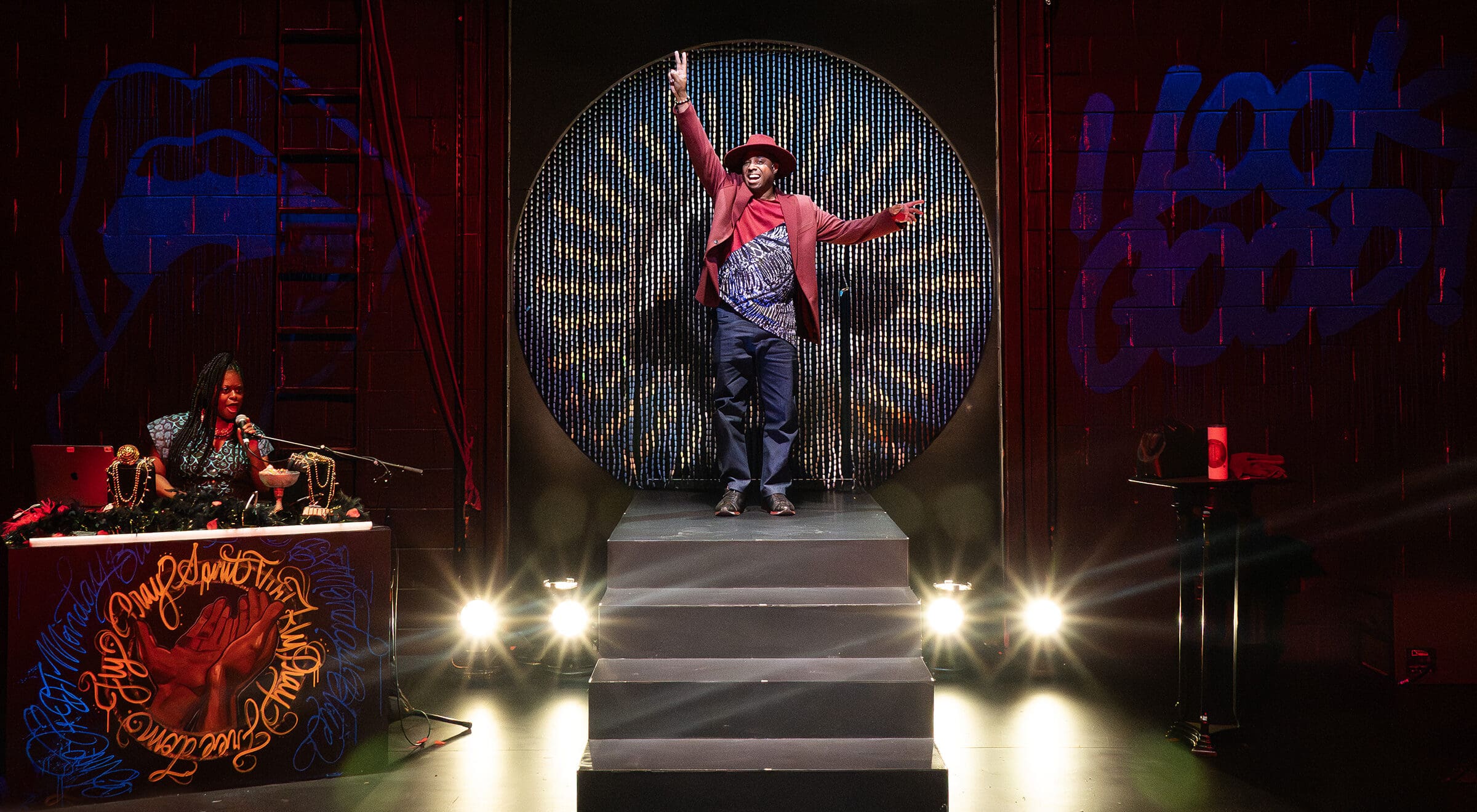 A performer on stage, arms raised, in front of a beaded backdrop. Community Audience Partnership shown on the DJ's setup.