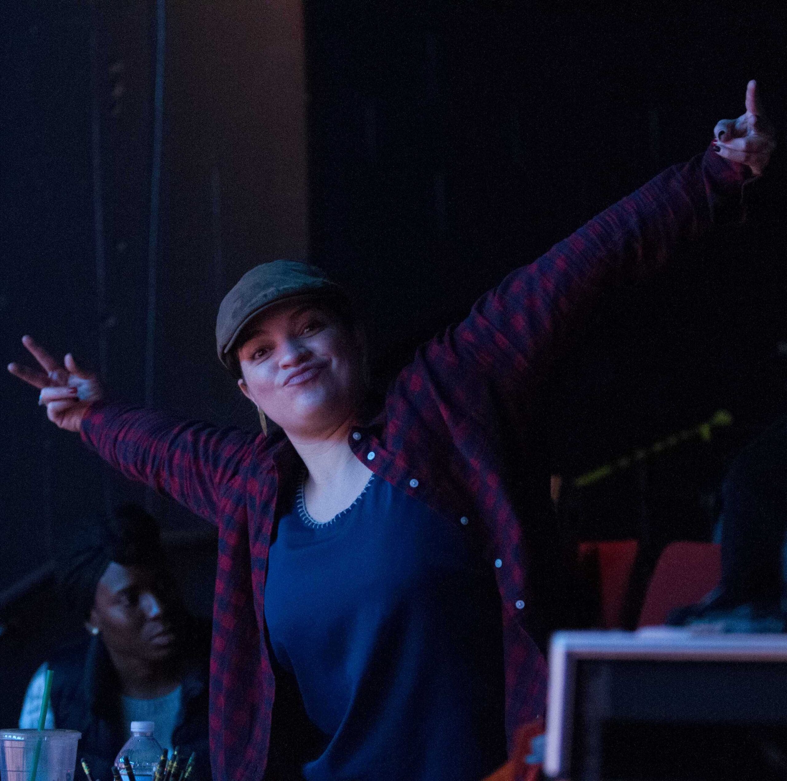 Woman in plaid shirt with arms raised, smiling. Stage setting.