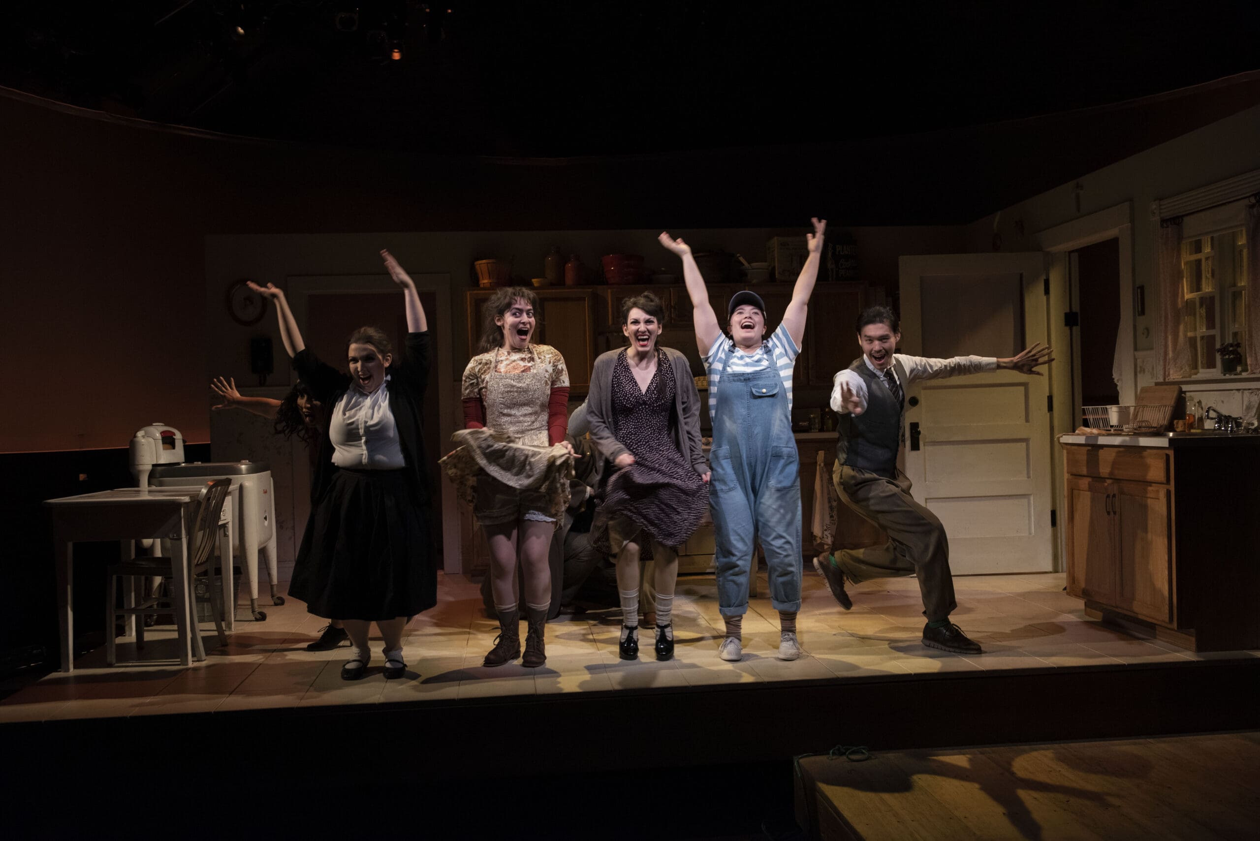 Actors in a theatrical performance on stage, arms raised in celebration.