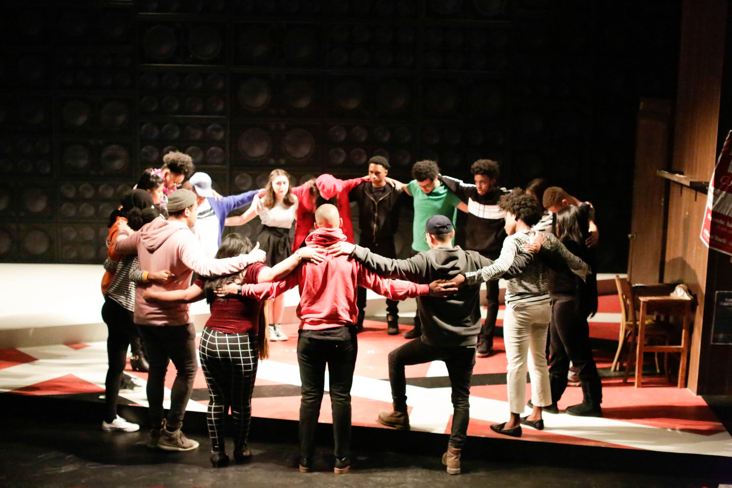 A diverse group of actors in a circle on a stage, arms around each other, embodying "Staging Success.