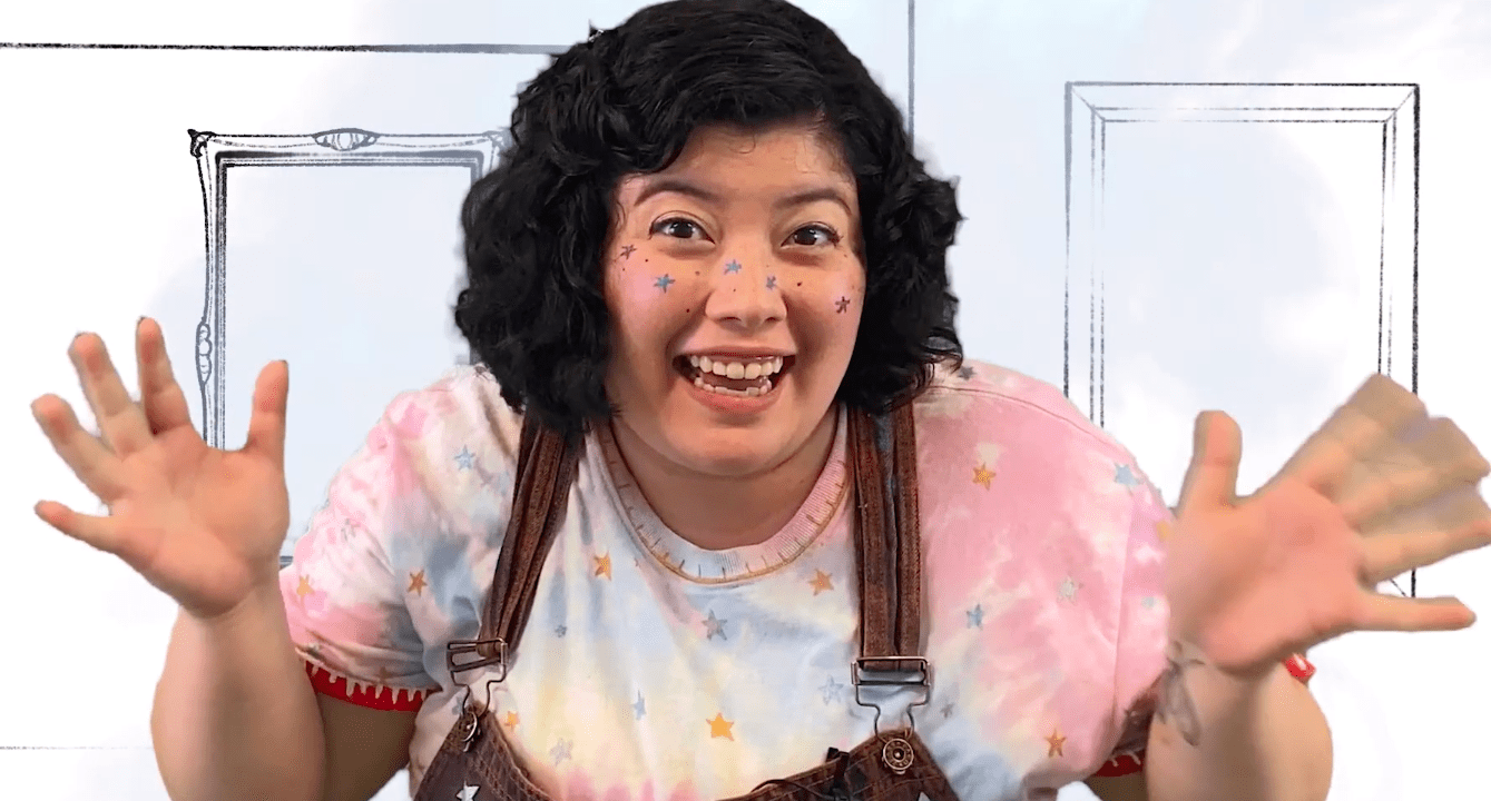 Smiling girl in overalls and star-print shirt, gesturing excitedly. Virtual production of "She Persisted, The Musical".