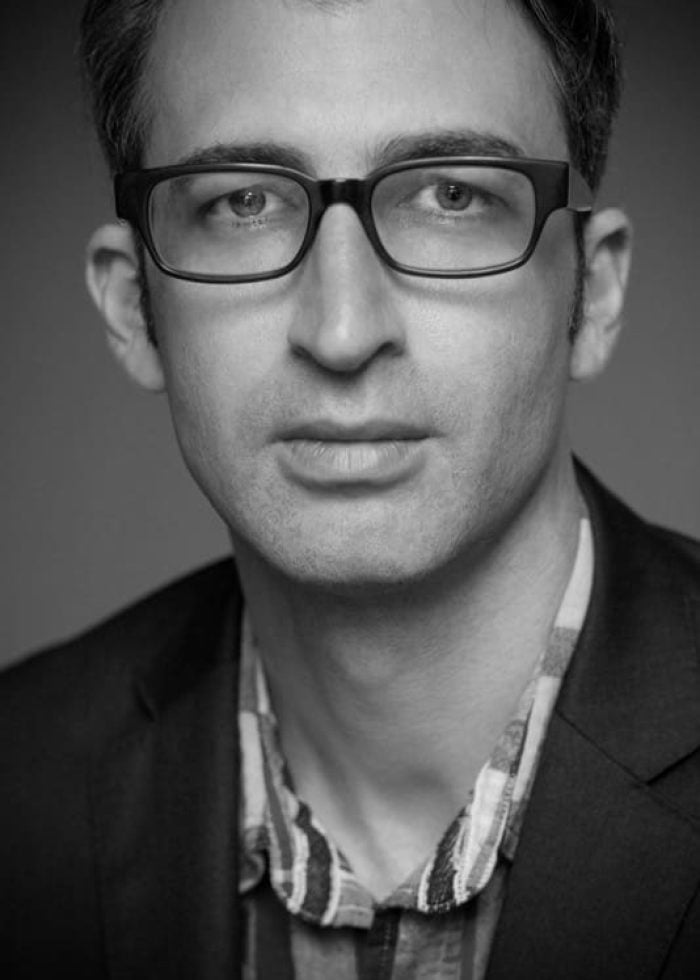 Daniel Aukin wearing glasses and a blazer, looking directly at the camera