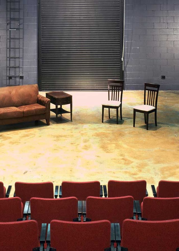 Small theater stage with red seats, sofa, chairs, and a rolling door backdrop.