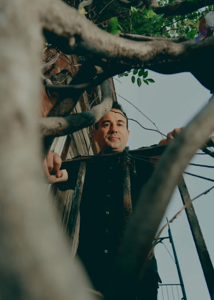 Man in black shirt framed by branches, possibly in a scene from "A Simulacrum.