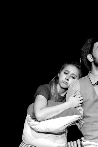 Black and white photo of a man and woman in theatrical costumes. The woman is hugging a pillow while the man gestures dramatically.