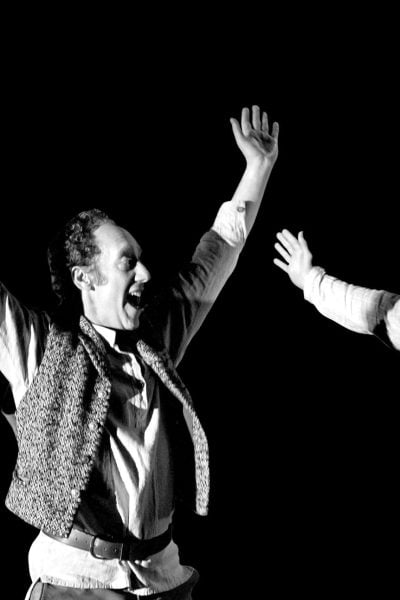 Two men in period costume perform a dramatic scene, arms raised.