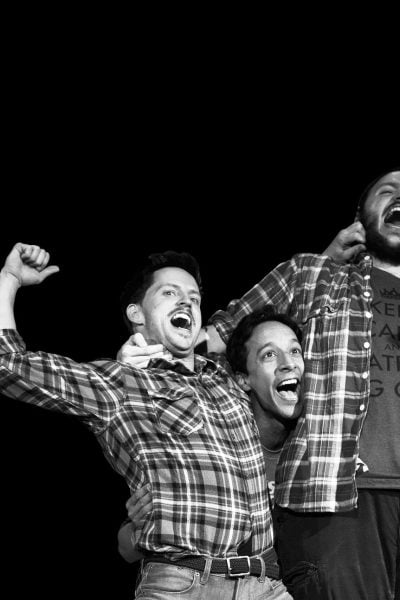 Four joyful men in plaid shirts, one wearing a "Keep Calm and Ate a Big Guy" shirt.