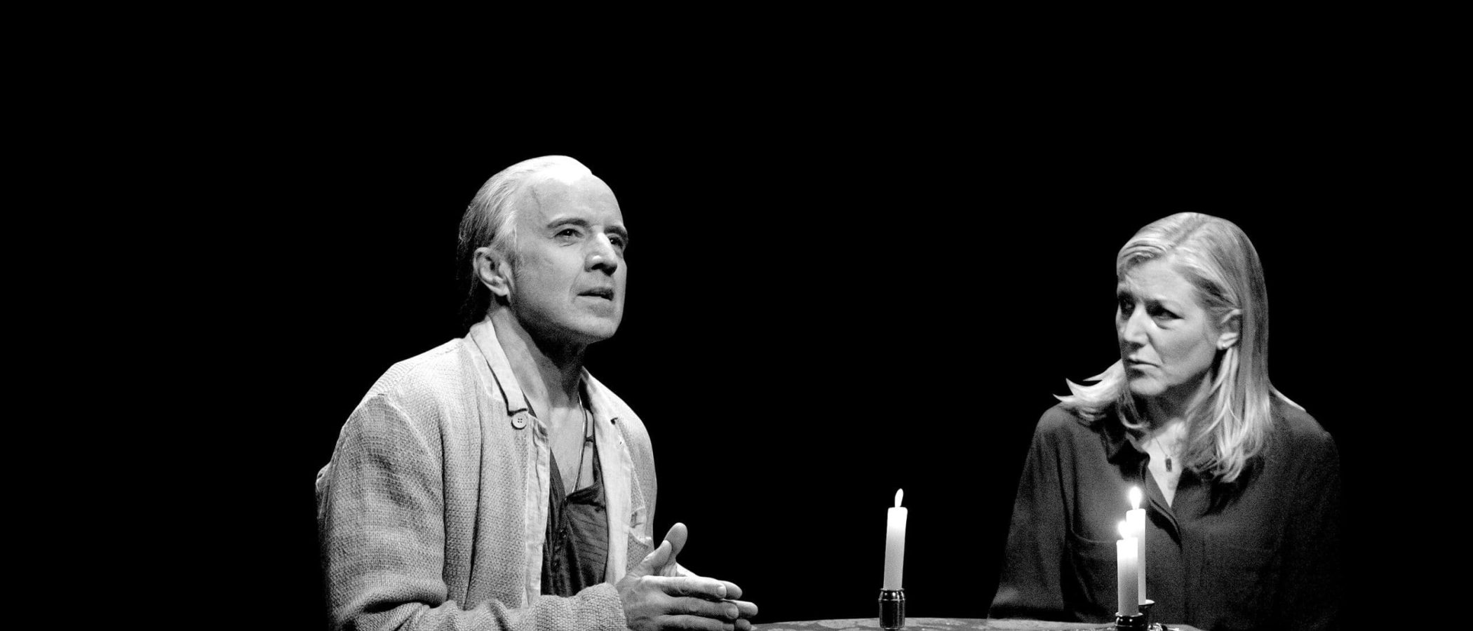 A man and woman sit at a table with lit candles, sharing a serious moment. Ghost stories.