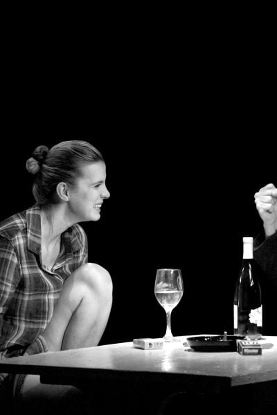Black and white photo of a man and woman having a tense conversation over wine and cigarettes.
