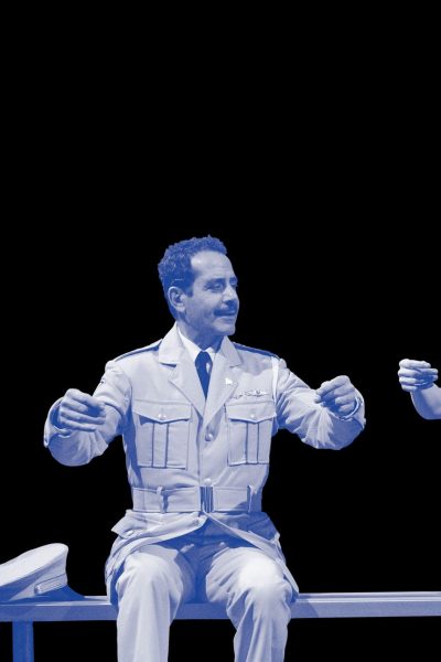 A man in a military uniform and a woman in a dress sit on a bench, facing each other in a scene from *The Band's Visit*.