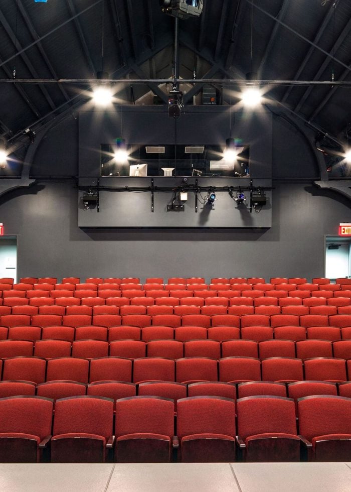 Theater interior with red seats and exposed brick walls.