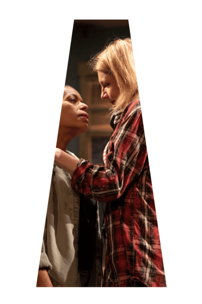 Two women embrace, one in a plaid shirt, the other in a muted green top.