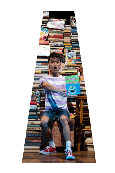 Young actor, surprised expression, holding "Monsters & Maniacs" book, surrounded by books.