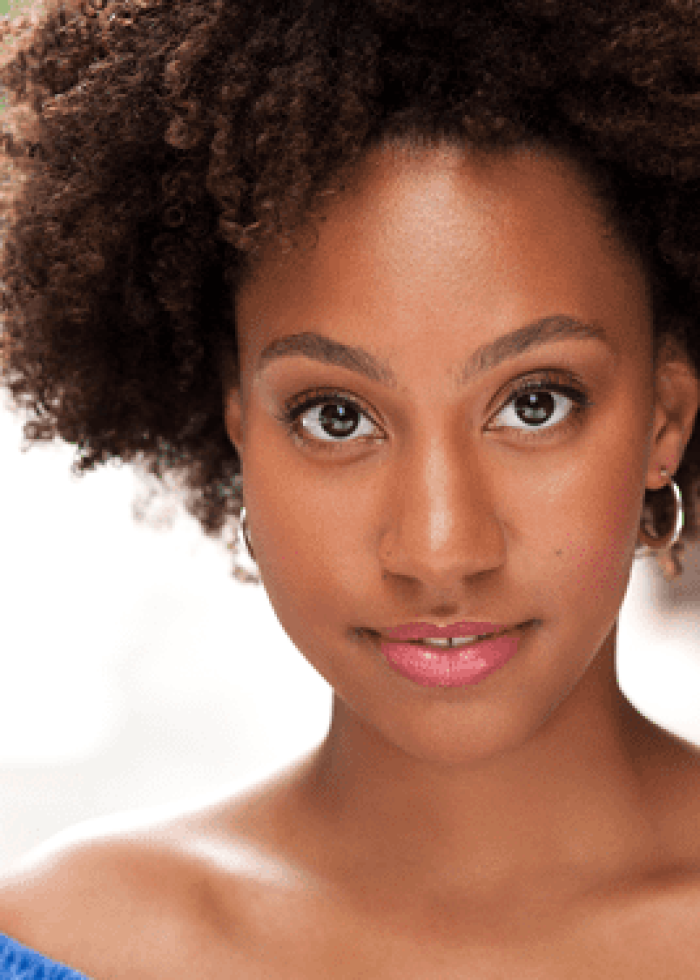 Regan Sims, a young woman with curly hair, smiles at the camera.