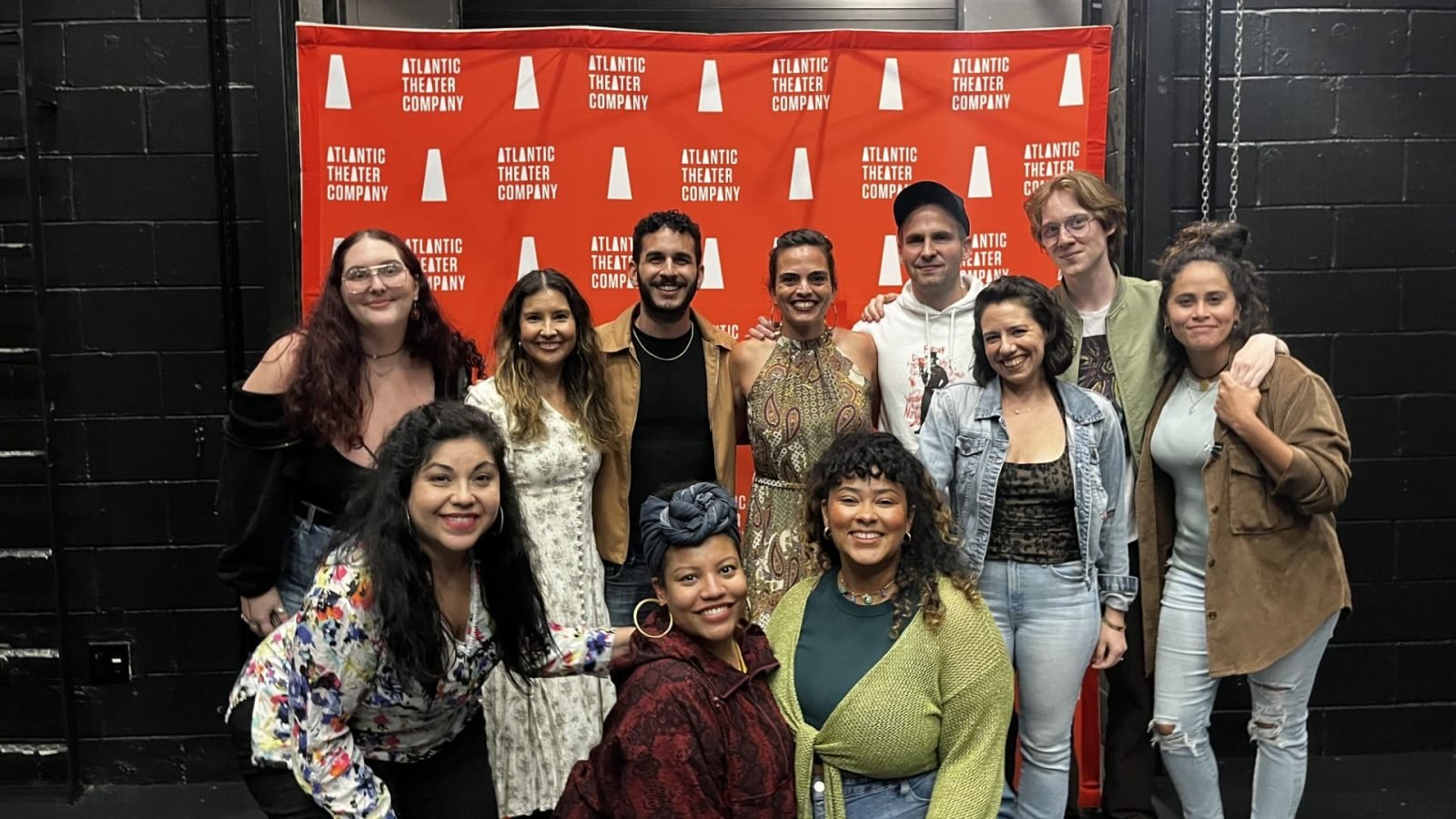 The cast of a new play pose in front of an Atlantic Theater Company backdrop.
