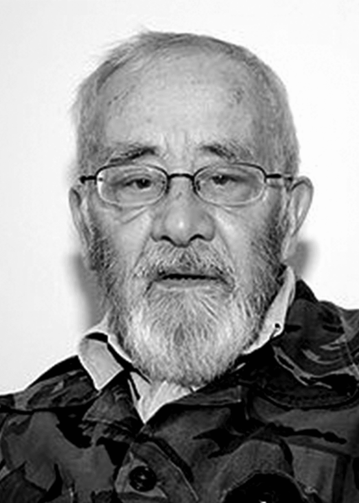 Portrait of an elderly man with glasses and a beard in a camouflage jacket.