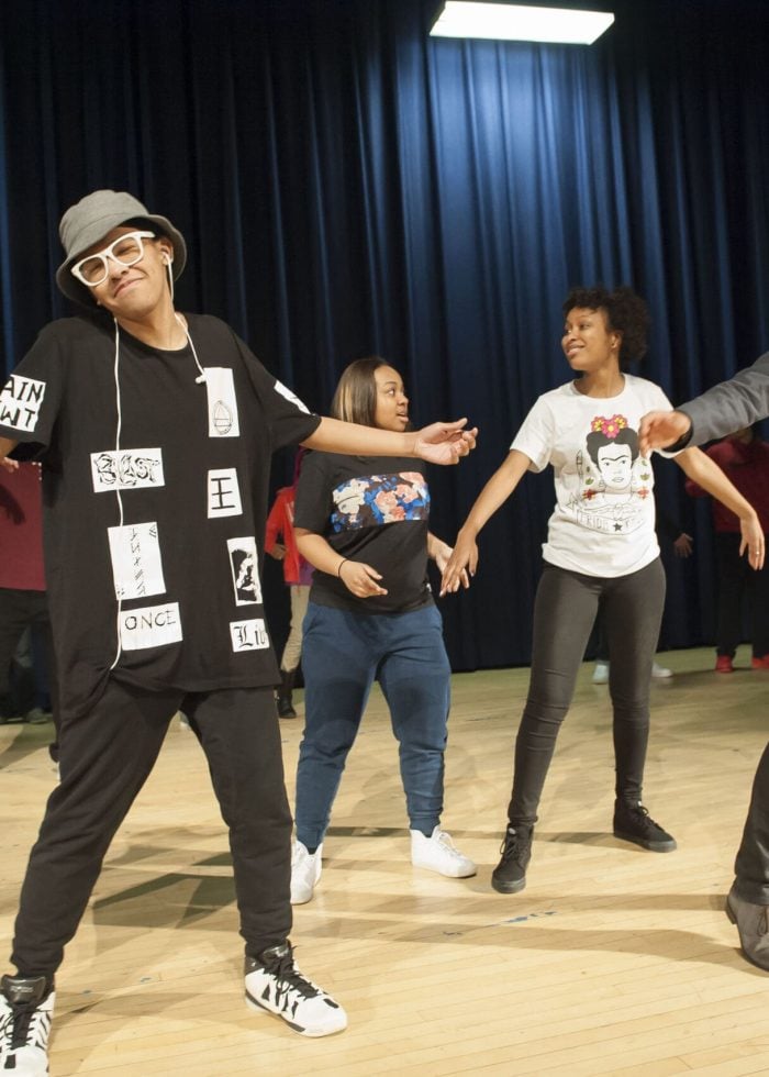 Dancers performing on stage, including a man in a suit and a woman in a shirt with text.