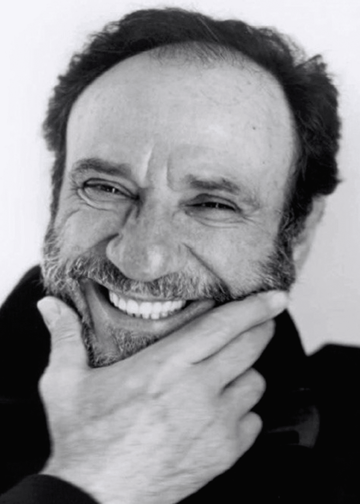 F. Murray Abraham smiling, hand on chin, black and white portrait