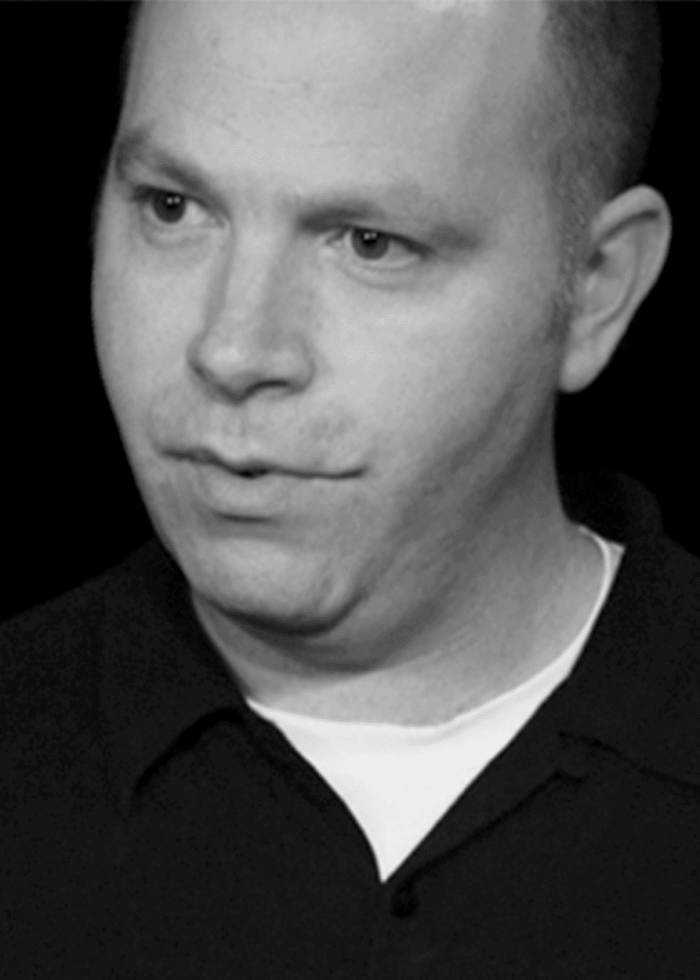 Adam Koplan in a close-up, looking thoughtful. Wearing a black shirt.