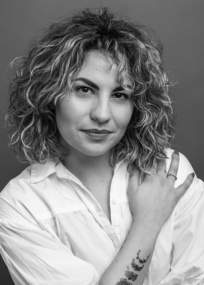 Alessandra Valea, a woman with curly hair, poses in a white shirt.