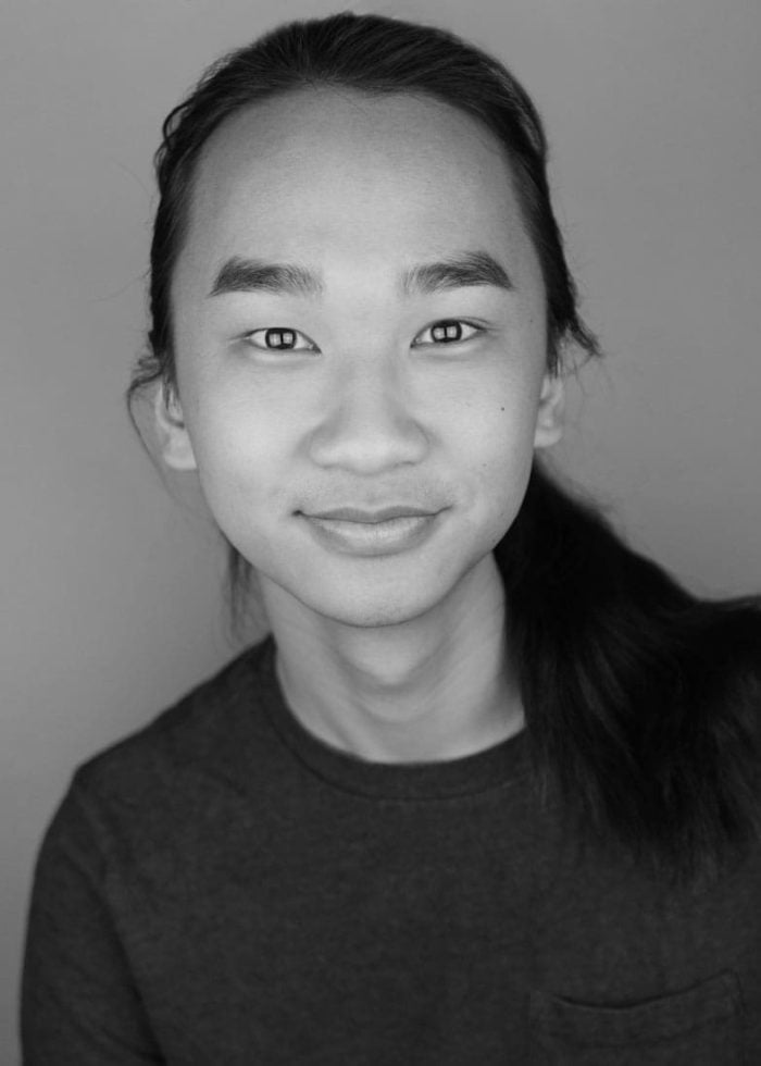 Alex Vinh smiling, with long hair in a ponytail, wearing a dark shirt.
