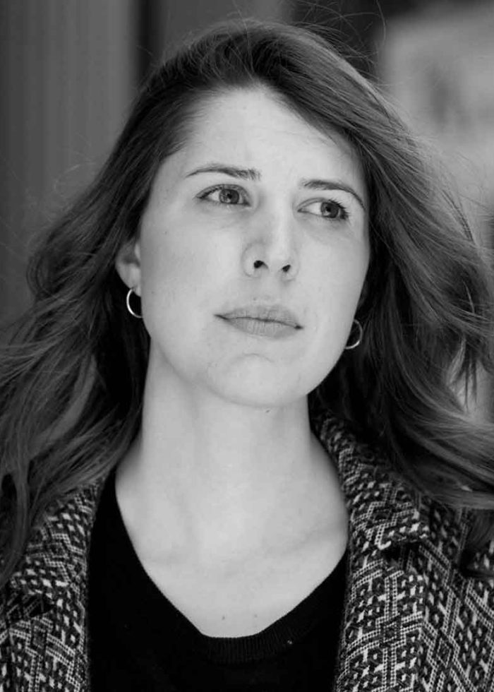 Alice Birch looks off camera, wearing a patterned coat and small hoop earrings.