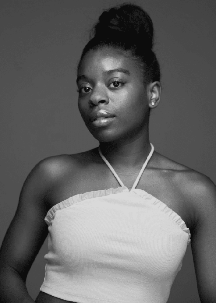 Young woman with a high bun wearing a white halter top, looking at the camera.