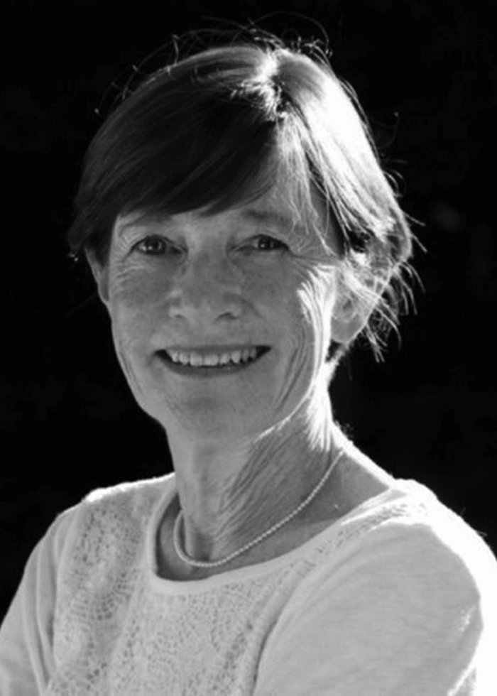 Ann McDonough smiling, wearing a white top and pearl necklace.