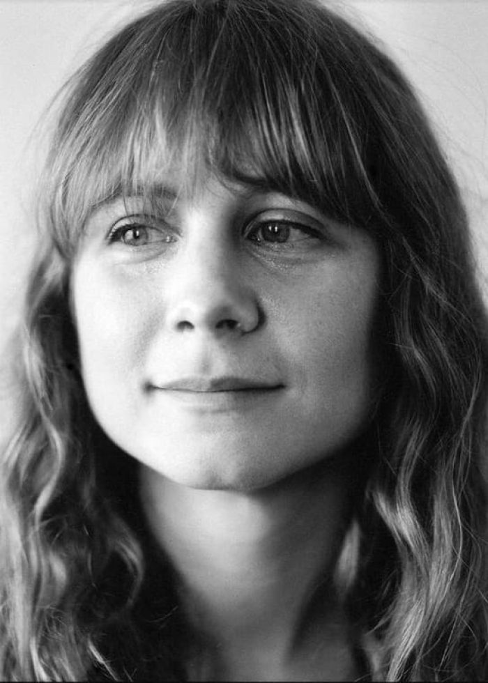 Portrait of Annie Baker with long wavy hair and bangs, looking thoughtful.