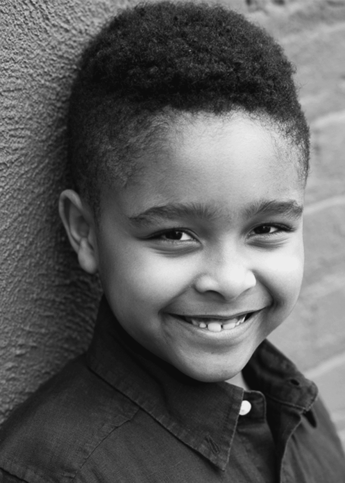 Young Antonio Watson smiles, leaning against a brick wall.