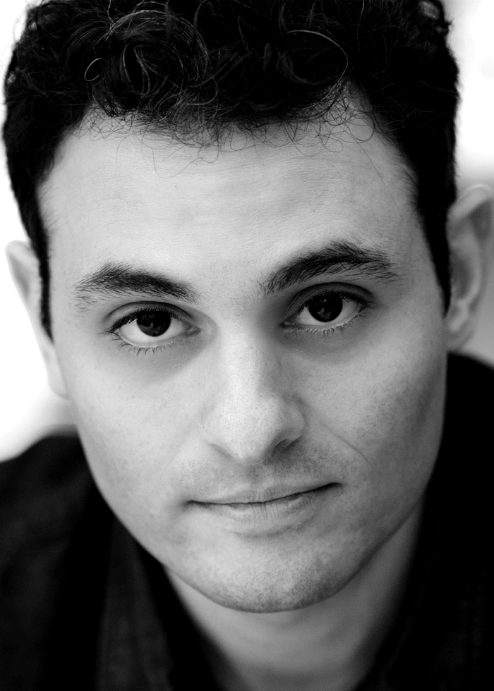 Arian Moayed looking directly at the camera in a black and white headshot.