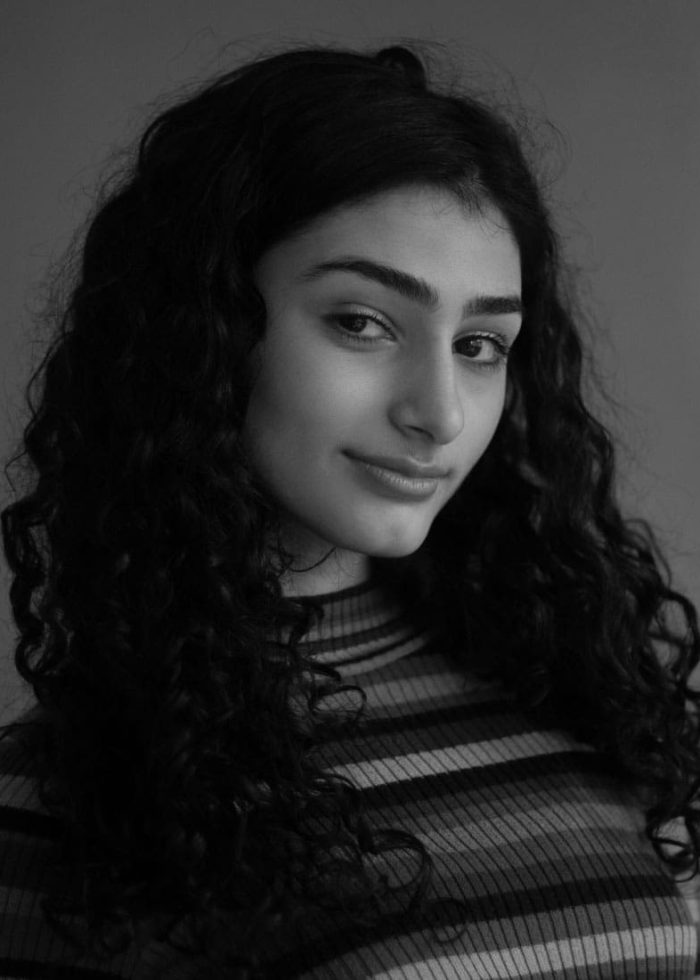 Portrait of Ava Lalezarzadeh with curly dark hair, smiling in black and white.