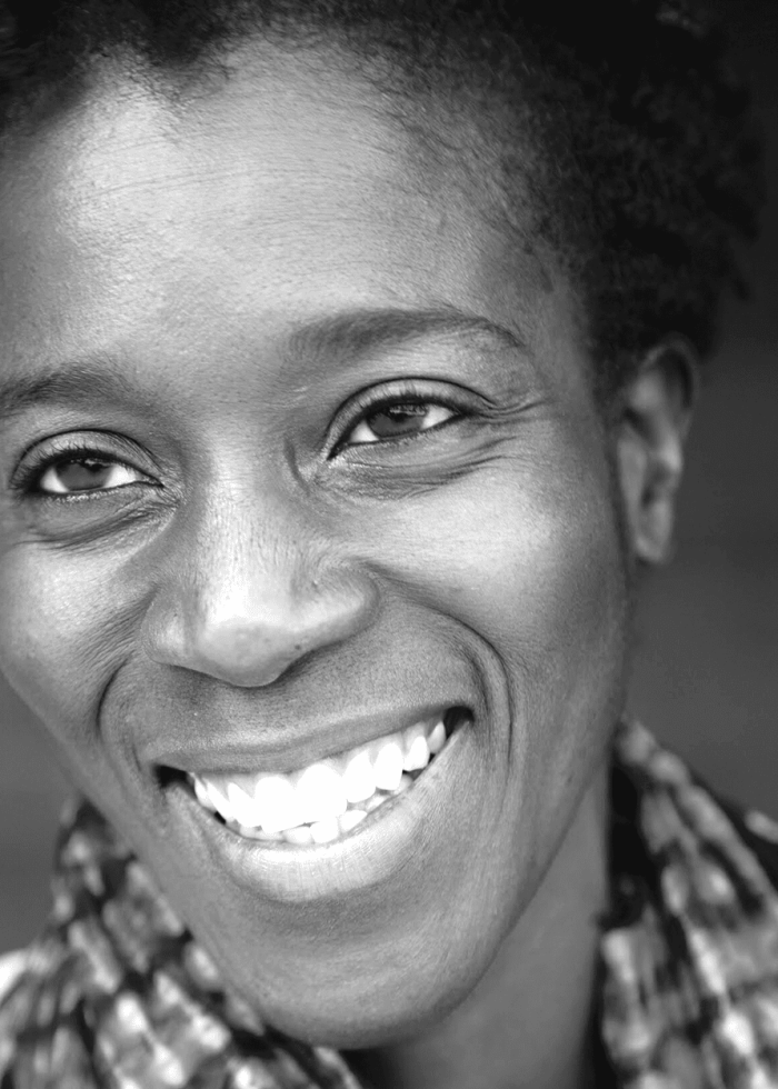 Awoye Timpo smiles warmly, close-up portrait in black and white.