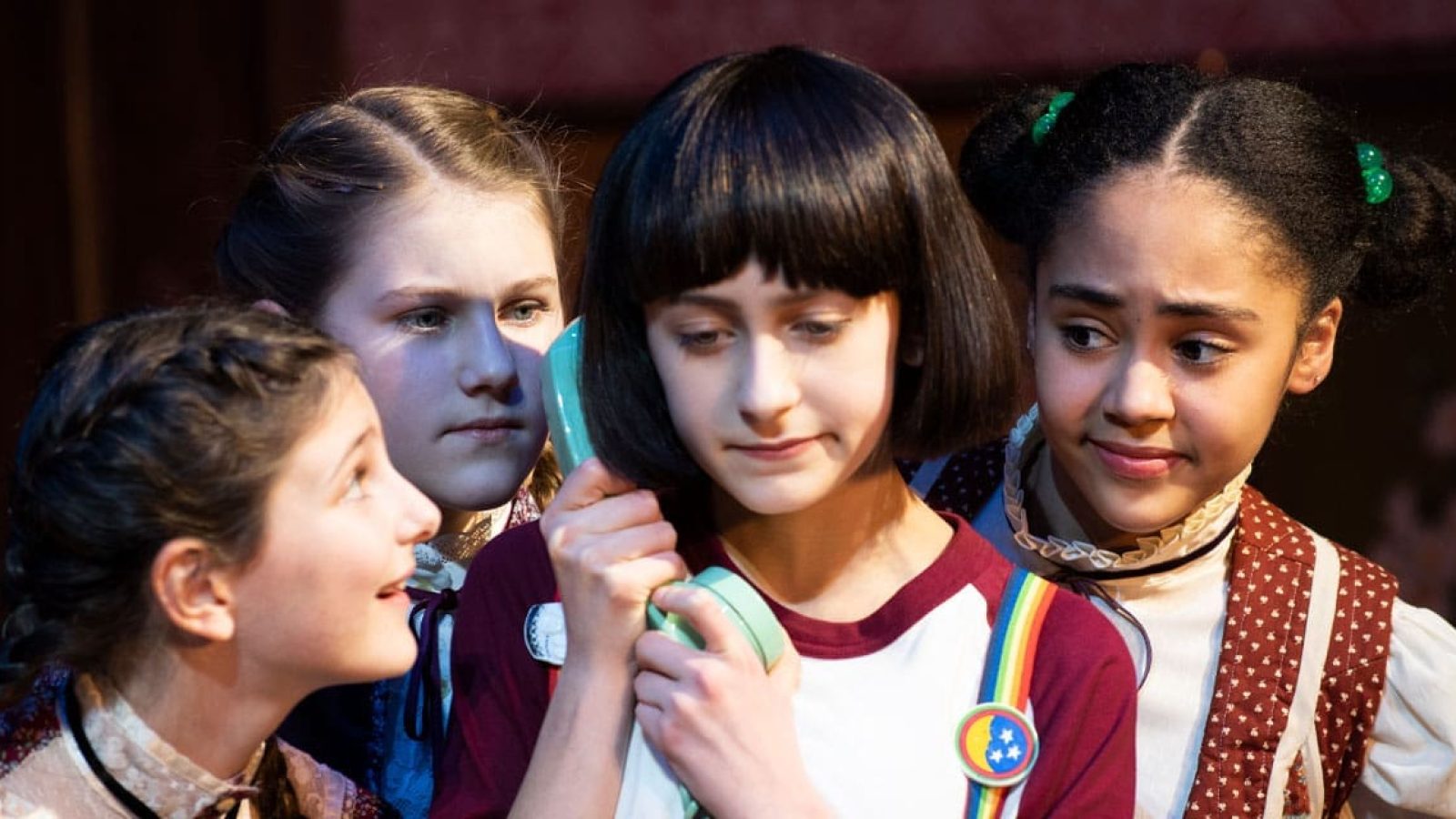 Four young actresses in period costumes share a vintage phone, whispering secrets. The Bedwetter.