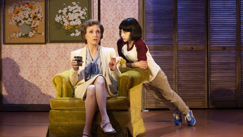 Woman in chair talking to child leaning on armrest in a stage play