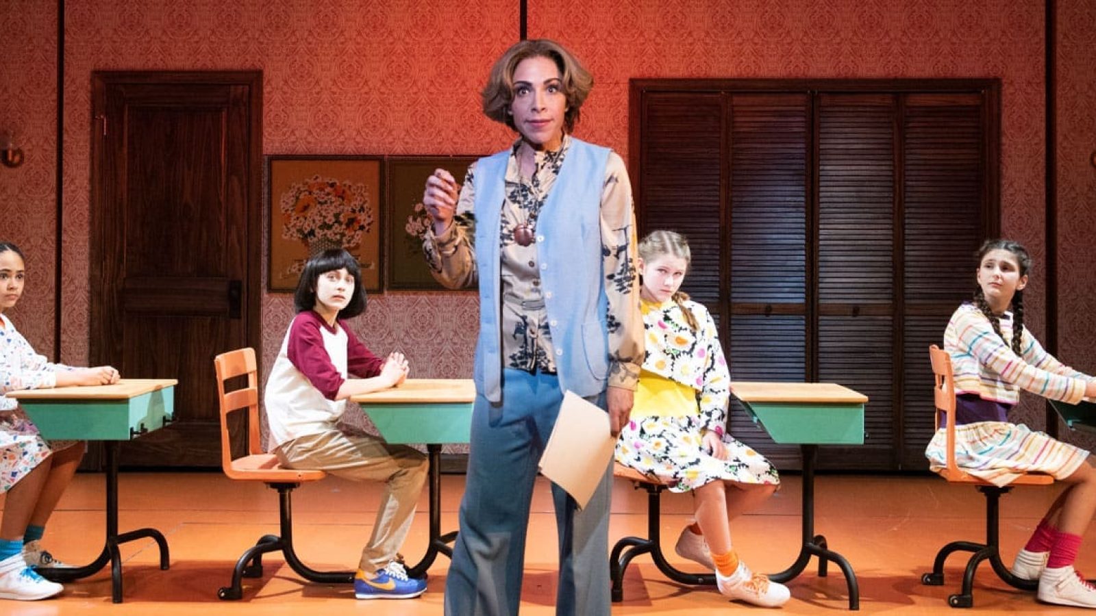 Cast of The Bedwetter, a musical, in a classroom scene. A teacher stands with four students at desks.