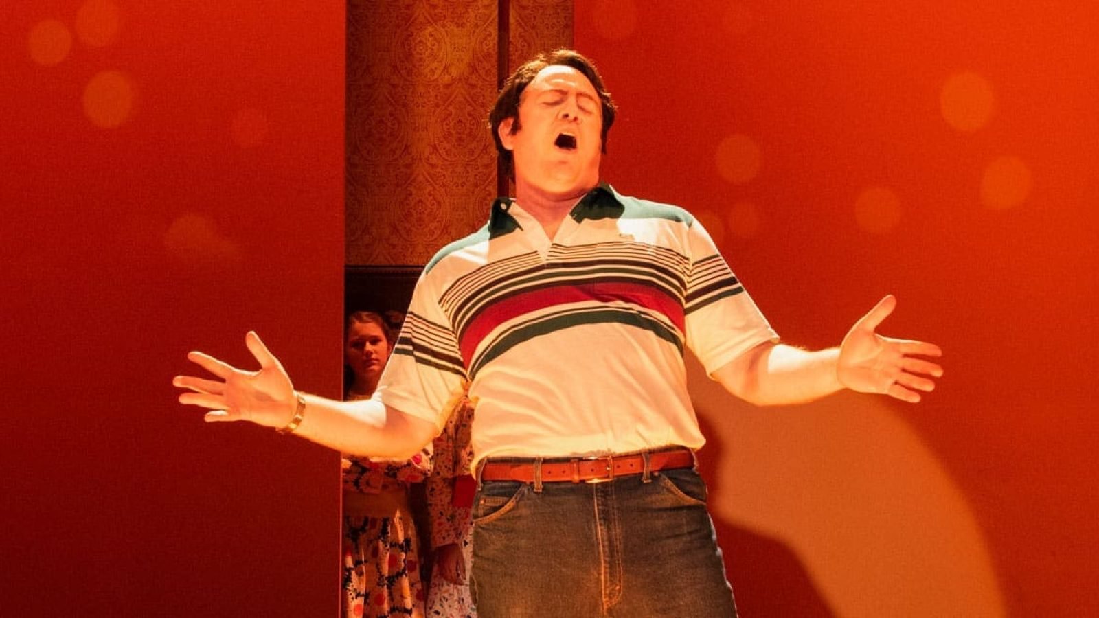 Man in 70s-style shirt singing passionately on stage