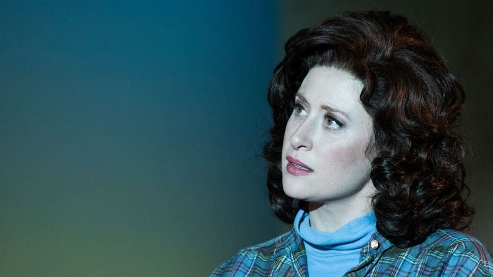 Close-up portrait of a woman with dark, curly hair, wearing a plaid shirt and turtleneck.