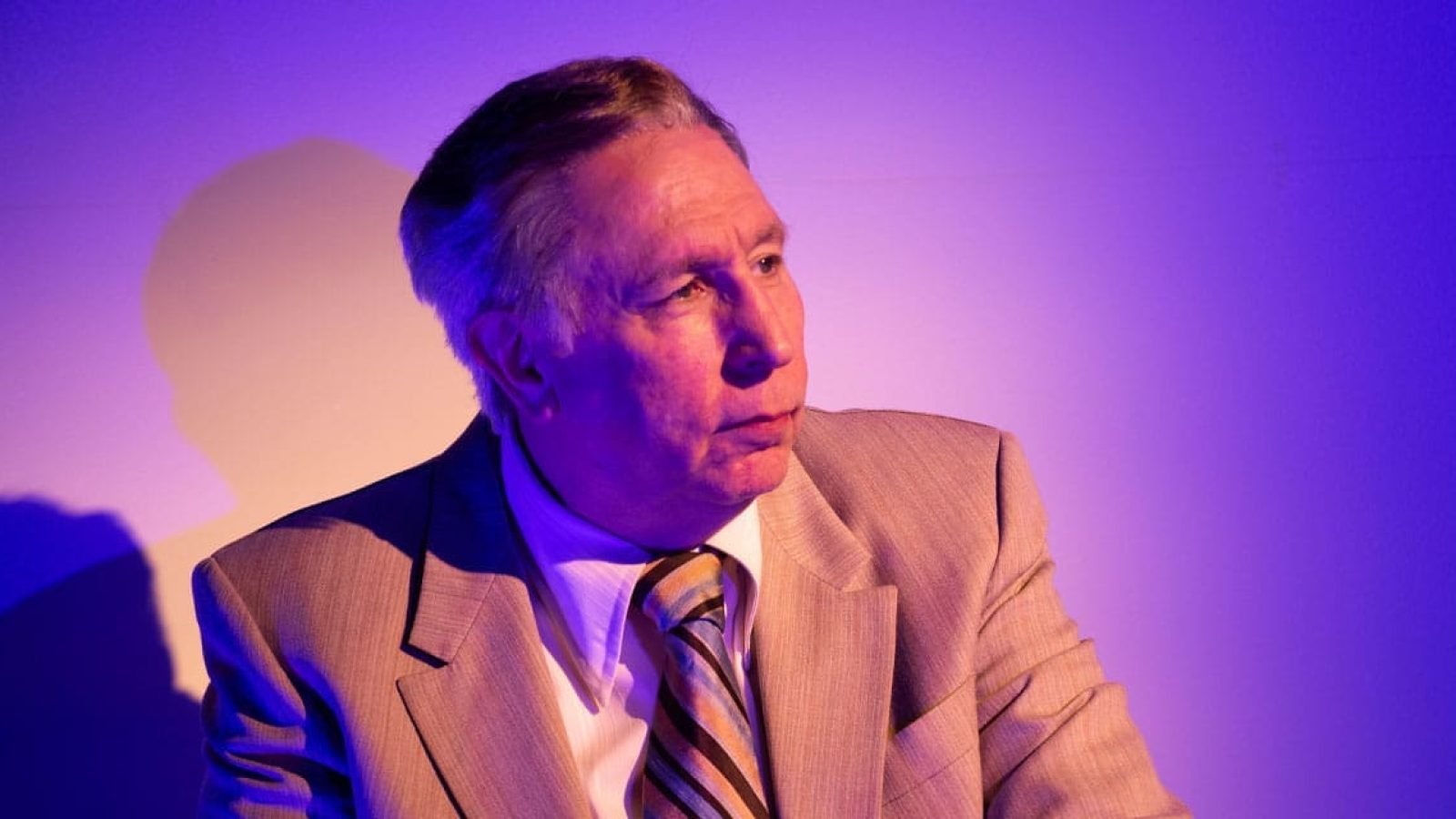 Portrait of a man in a beige suit, looking thoughtfully to his right.