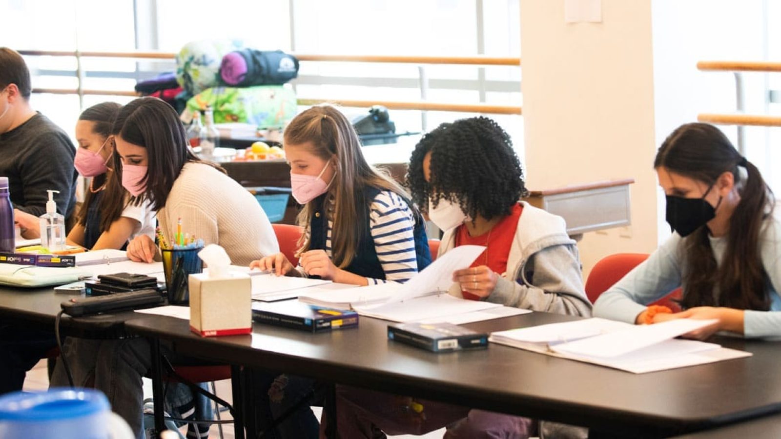 Students wearing masks work at tables during a rehearsal.