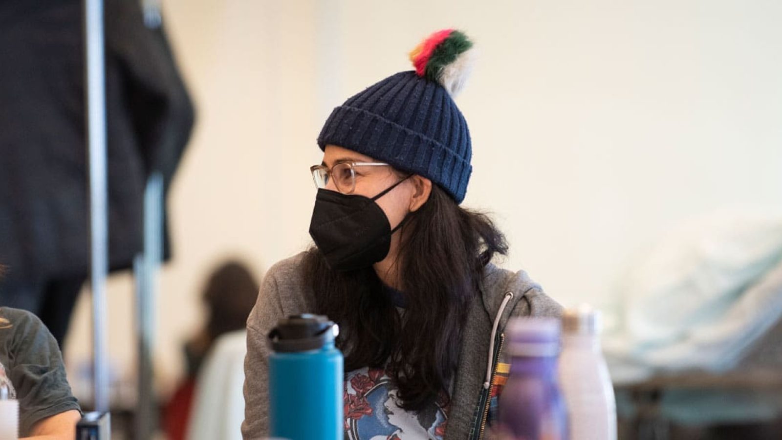 Woman wearing a knit hat and face mask, attending a meeting.