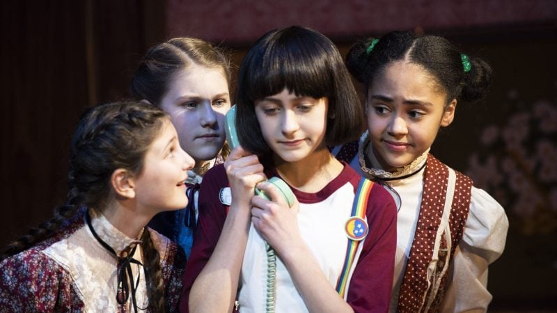 Four young girls in vintage outfits, one holding a vintage telephone, possibly discussing membership.