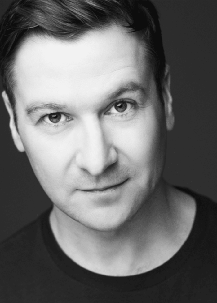 BILLY_CARTER_Final_edit_headshot_1 Close-up portrait of a man with short dark hair, looking directly at the camera.