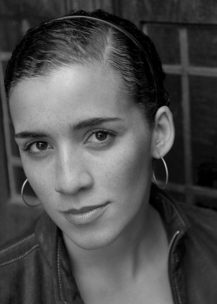 Woman with dark hair, hoop earrings, and jacket, looking at the camera.