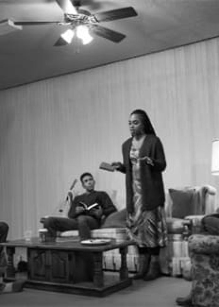 Group of people in a community discussion; a woman speaks while others listen. Keywords: patriarchy, activism.