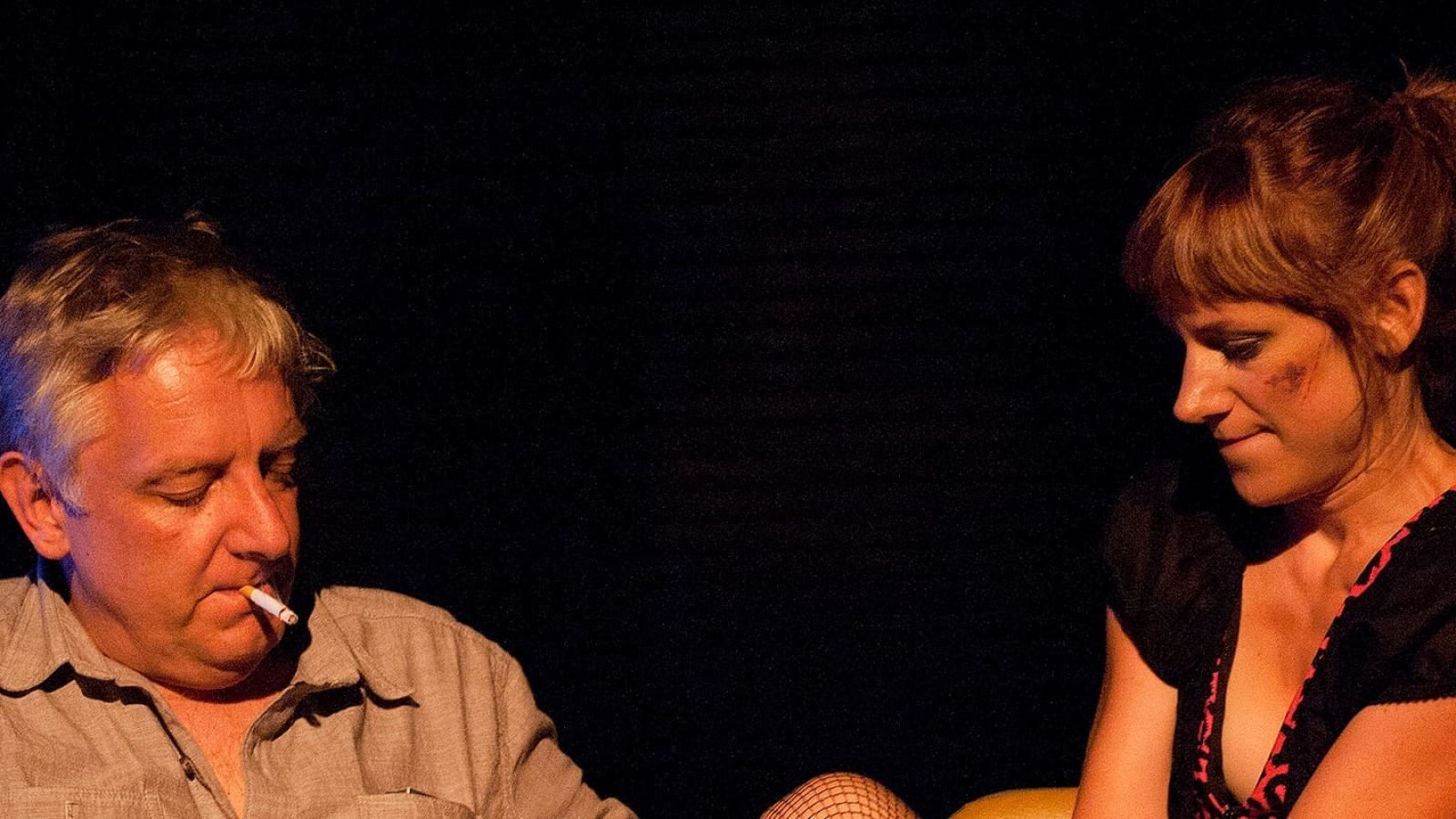 Man and woman in dimly lit setting; she has a bruise.