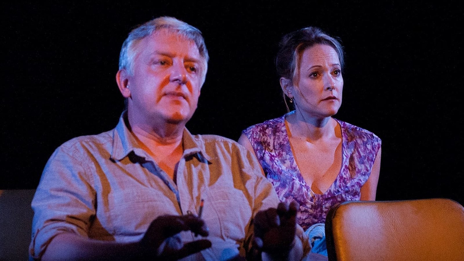 A man and woman sit in chairs, appearing concerned.