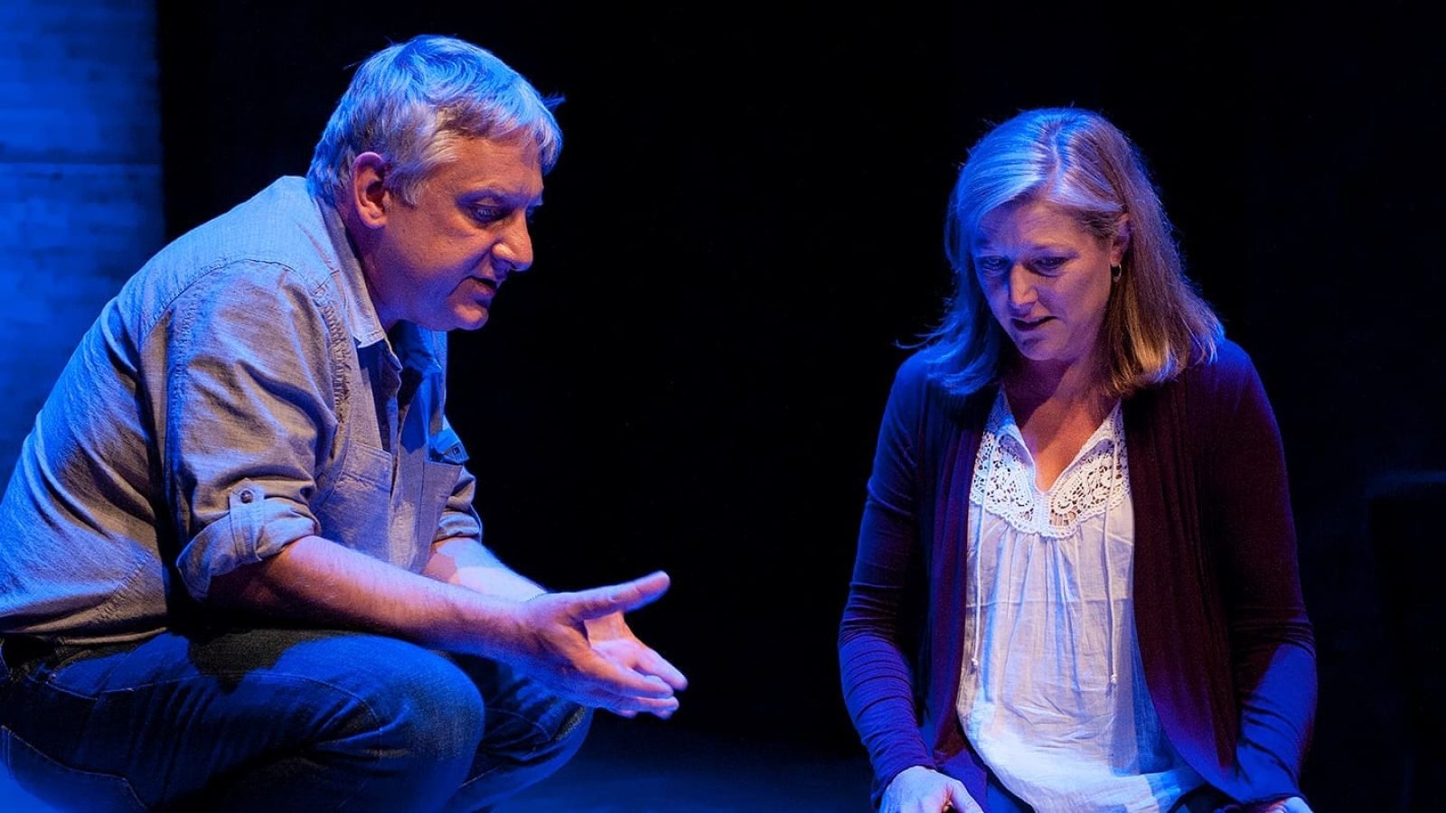 Man and woman in a serious conversation on stage under blue light